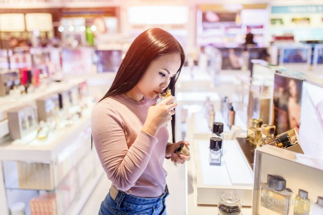 Young asian woman testing and choose to buy perfume in duty free store at international airport.