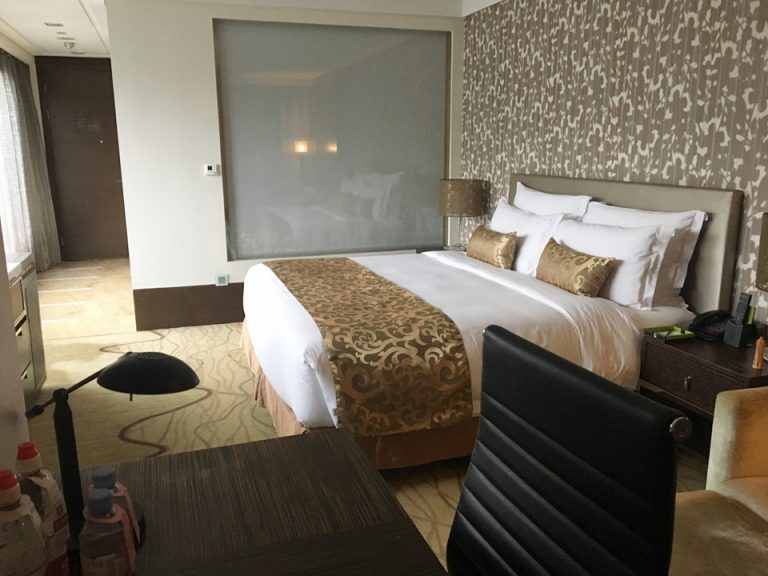 部屋の奥の窓側から客室を見た様子。手前にライティングデスクと一人掛けソファがあり、ベッドの奥がバスルームです。