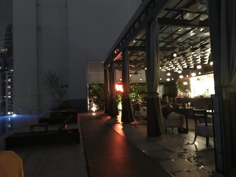 夜のプールサイドです。プールに面したバーではお客さんが飲食を楽しんでいます。音楽が流れ、開放的な雰囲気です。