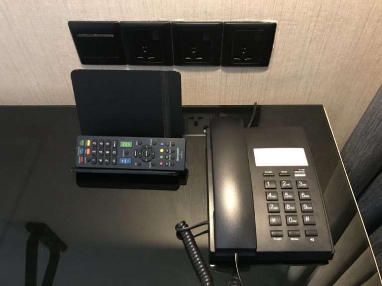 デスク3 デスク周りです。電源3つと、デスクライトの電源が並び、電話機とTVリモコンです。