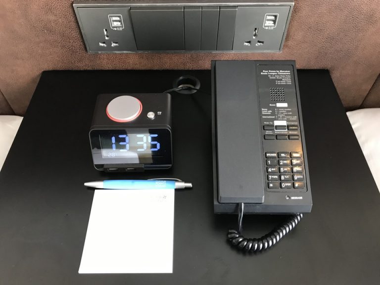 ベッドサイドの机の上です。USB電源付きのアラーム付きの置き時計、電話と電源コンセントとUSB電源、部屋の明かりのスイッチがありました。